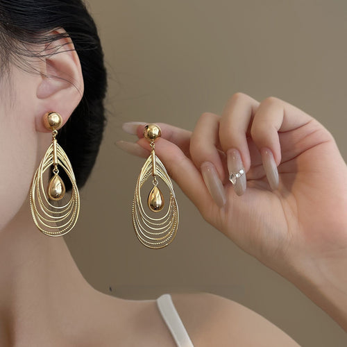 Nested open teardrop outlines suspended from round gold-tone studs shown in a styled close-up