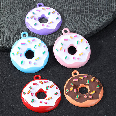 Five enamel donut charms in purple, blue, pink, red and chocolate brown with colorful sprinkles on gray textured fabric