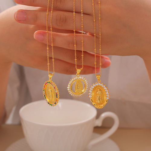 Three gold Virgin Mary zircon pendants held above white cup
