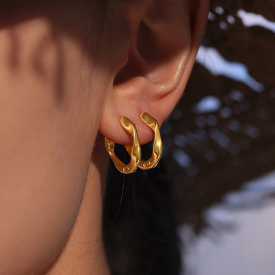 Gold twisted irregular mini huggie hoops worn on ear