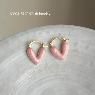 Pink enamel heart huggie hoops on white ceramic plate surface