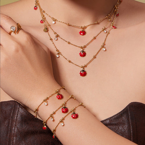 Model wearing layered gold ladybug necklaces and bracelets