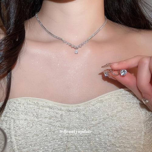 Silver graduated CZ teardrop necklace worn with ear clip held near collarbone
