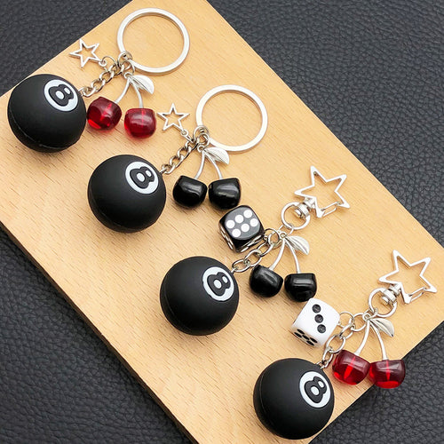 Grouped four black 8 ball keychains with dice and cherries arranged together on a styled display surface
