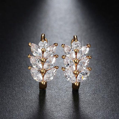 Gold marquise leaf wheat huggie earrings upright on dark surface
