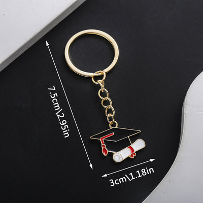 Front product photo of black graduation cap and diploma enamel charm keychain showing the pictured design arrangement