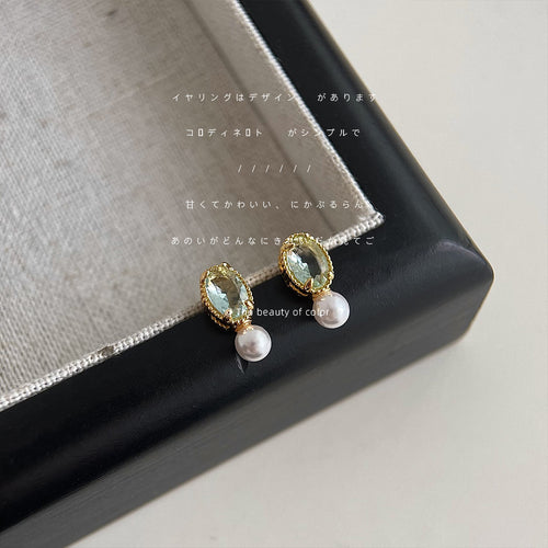 Gold-tone pale-green-oval-stone white-pearl studs shown worn on an ear.