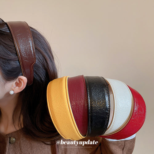 Brown faux leather headband worn while holding multi-color headband stack