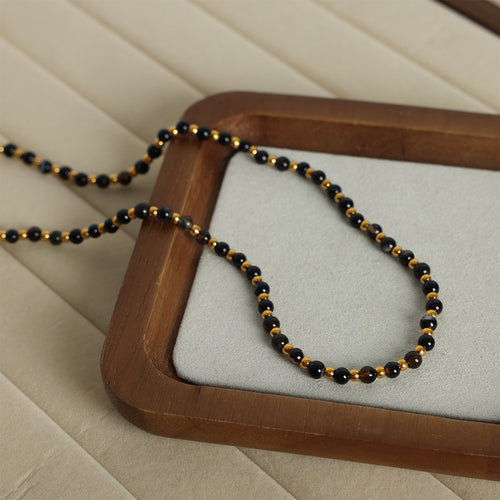 Small black and gold bead necklace looped on wooden tray with velvet pad