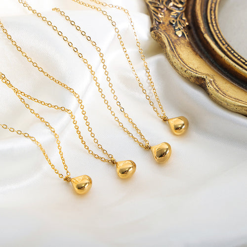 Several gold teardrop pendant necklaces laid on white fabric by gold frame