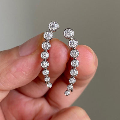 Silver graduated clear CZ ear climbers held between fingers front