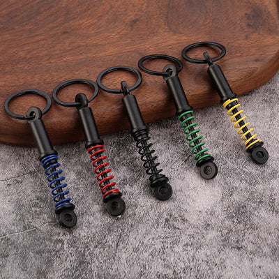 Five miniature shock absorber keychains with blue, red, black, green, and yellow coil springs.