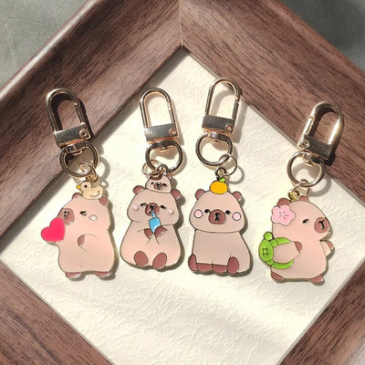 Four enamel capybara keychain charms with gold lobster clasps in wooden tray