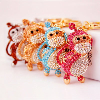 Four monkey keychains displayed in pink, blue, peach, and brown tones.