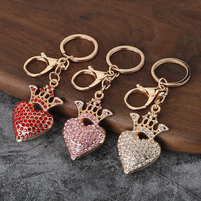 Three gold-tone crowned heart keychains with red, pink, and clear rhinestones on a wood surface.