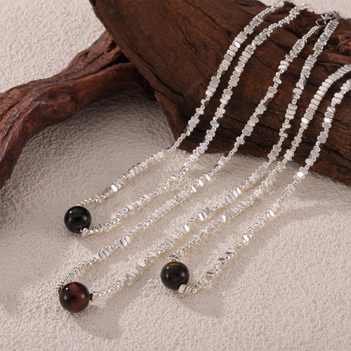 Three silver chip bead necklaces with tiger-eye spheres on sand and wood
