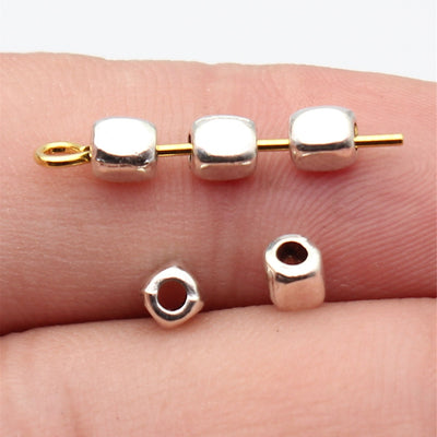Tiny polished cube spacer with a centered stringing hole shown close up on a hand