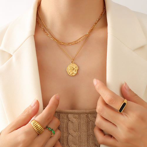 Close gold layered coin medallion necklace on model hands framing chest