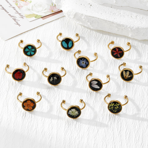 Eleven gold open dried flower resin cabochon rings arranged on white cloth