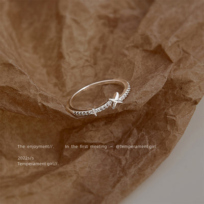 Silver-tone clear-stone star crossover open ring on crumpled brown paper.