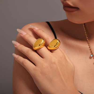 Model wearing two chunky gold polished dome rings on hand near shoulder