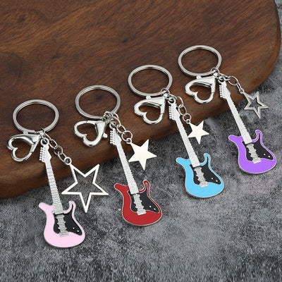 Five colored guitar keychains with mixed solid and outline star charms on gray fabric.