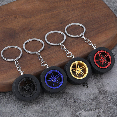 Four black tire keychains with black, blue, gold, and red wheel inserts on a wooden surface.