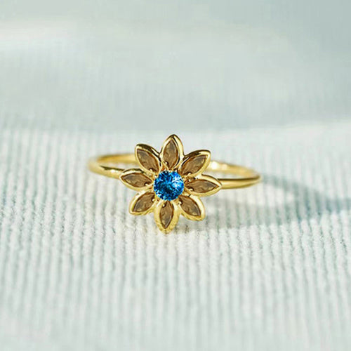 Angled detail view of gold tone flower ring with blue center and green petals