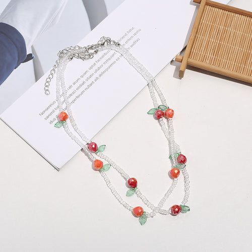 Layered clear seed bead necklace with red fruit-shaped charm beads and green leaf accents
