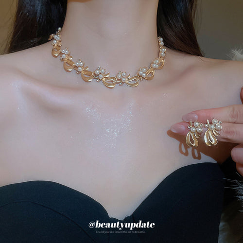 Gold pearl bow necklace worn with matching stud earrings held in hand