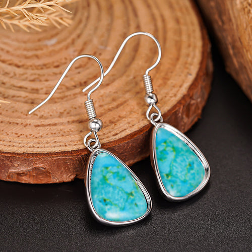 Silver turquoise teardrop drops on wood slice dark surface angled