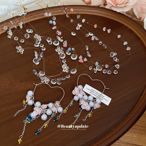 Clear flower necklace pink chip necklace and heart flower hoop earrings on wood tray
