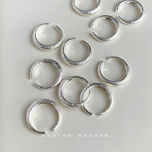 Multiple silver frosted open adjustable rings scattered on cream surface