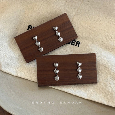 Silver triple heart drops on wooden cards over beige cloth