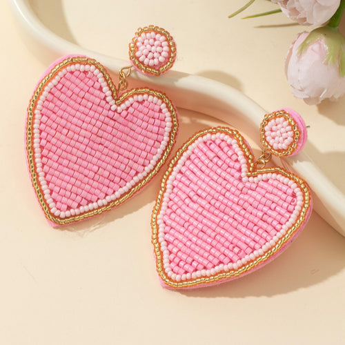 Pink heart beaded drop earrings shown on cream background with pink flowers nearby