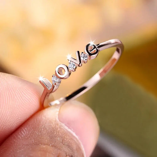 Rose gold LOVE letter ring held between fingertips close-up