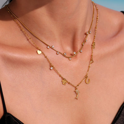Gold dolphin multi-charm necklace layered on collarbone with second chain
