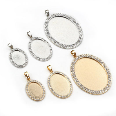 Overview of oval pendant trays edged with clear crystals in bright silver and gold-tone finishes arranged on a light bac