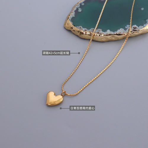 Gold puffy heart necklace flat on gray with length and style labels