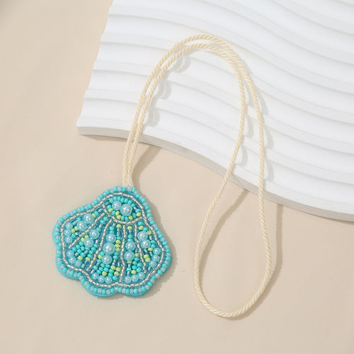 Turquoise beaded pearl seashell charm pendant hanging from a cream cord on a beige background