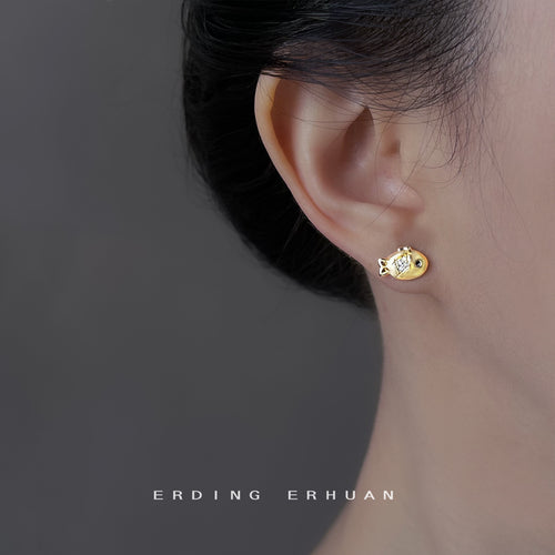 Gold fish stud earring worn on ear close-up side profile