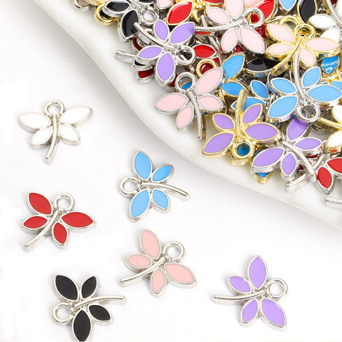 Assorted four wing enamel dragonfly charms arranged beside a tray on white