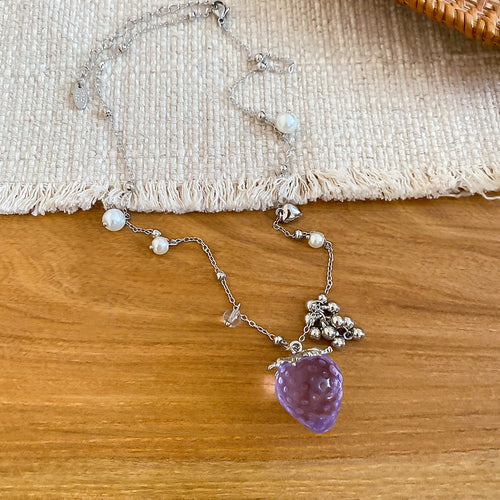 Silver pearl chain necklace with purple strawberry pendant on wood