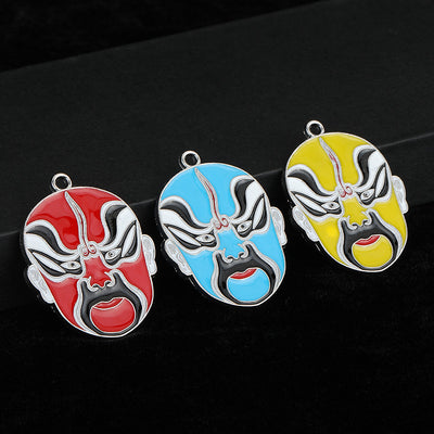 Three Peking opera mask enamel charms in red, blue and yellow arranged on a dark cloth