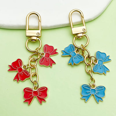 Red and blue three-bow keychains displayed on a pale green surface.