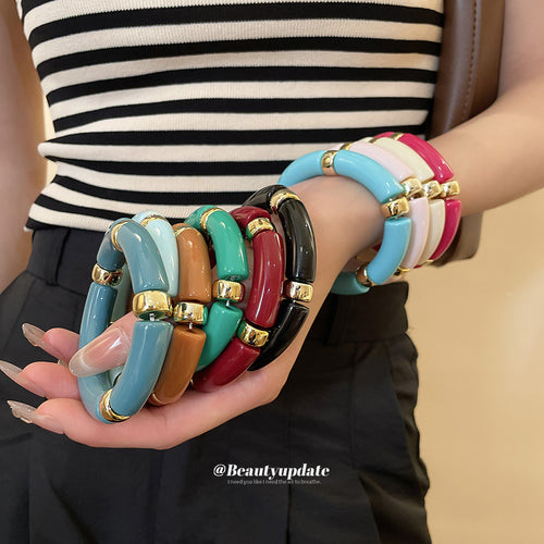 Model arms stacked with many acrylic tube gold-spacer bracelets