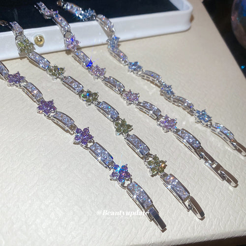Four silver flower link bracelets laid out showing box clasps on cream surface