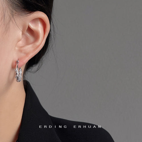 Silver-tone clear-stone leaf-pattern hoops shown worn on an ear.