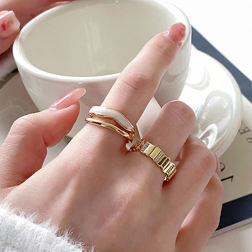 three unrelated gold-tone ring designs with white and geometric details shown in the first close product view