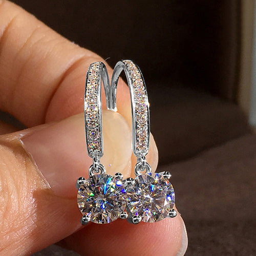 Silver tone round clear drop leverback earrings held between fingers